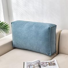 a blue pillow sitting on top of a white couch next to a book and potted plant