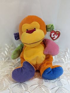 a stuffed monkey sitting on top of a white lace covered tablecloth with a tag