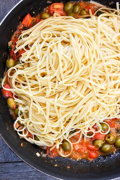 a pan filled with pasta and olives on top of a wooden table