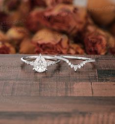 two engagement rings sitting on top of a wooden table next to red rose petals in the background