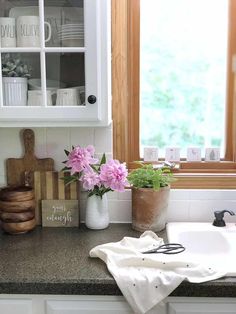 a kitchen counter with flowers and utensils sitting on it's side, next to a window