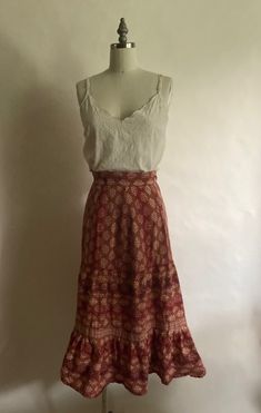 "1970s 100% cotton print skirt with drawstring at the waist and bottom hem ruffle was made in India. In excellent vintage condition. Waist up to 28\" Hips 38\" Length 29\":" Boho Skirt And Sweater Outfit, Ruffled Cotton Maxi Skirt, Cotton Maxi Skirt With Ruffle Hem, Vintage Red Ruffled Skirt, Cotton Peasant Tiered Skirt, Bohemian Skirt With Ruffle Hem And Flowy Fit, Vintage Red Skirt With Ruffles, Vintage Red Tiered Skirt, Bohemian Flowy Skirt With Ruffle Hem