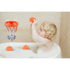 a young child in a bathtub playing with a basketball hoop and ball set on the rim