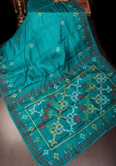 Step into elegance with this Teal Gachi Tussar Silk Saree, featuring exquisite hand embroidery that showcases traditional craftsmanship. The saree is crafted from luxurious Gachi Tussar silk, known for its rich texture and natural sheen, highlighted by a captivating teal hue. Adorned with intricate hand embroidery, the saree displays delicate patterns that add a touch of sophistication and artistry. Complementing the embroidery are detailed Pitta work and mirror accents, which bring a subtle sparkle and enhance the saree's overall allure. Perfect for special occasions and festive celebrations, this saree seamlessly blends classic artistry with contemporary elegance, making it a standout addition to any wardrobe. Ready to wear with fall and pico done. An unstitched blouse fabric is included