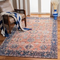 an orange and blue area rug in a living room with a chair, vases and window