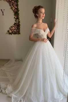 a woman in a white wedding dress standing next to a wall with flowers on it