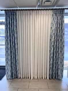 an open window with blue and white curtains in front of it on tile flooring