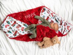 a baby wrapped in a blanket laying on top of a bed next to a teddy bear