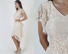 "Vintage 80s sheer ivory floral lace dress. V neck wrap style bodice with fluttery sleeves. Gathered and fitted waist with sweeping, tulip hi lo skirt. Dress is lined and zips up the back. size estimate: S shoulders: 17.5\" bust: 30\" waist: 28\" hips: 30\" total length: 35\"-42\" Model is 5'9\" and measures 33\" bust, 25\" waist, 33\" hips. Belts/accessories are not included unless noted in the description." Fitted Short Sleeve Delicate Lace Dress, Fitted Short Sleeve Lace Dress With Delicate Lace, Delicate Lace Fitted Dress With Short Sleeves, Fitted Lace Dress With Ruffles For Wedding Guests, Fitted V-neck Lace Dress For Wedding Guest, Short Sleeve Cream Lace Dress, Cream Short Sleeve Lace Dress, Fitted V-neck Lace Dress With Delicate Lace, Vintage Lace V-neck Dresses