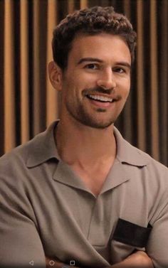 a smiling man with his arms crossed in front of a curtained wall, looking at the camera