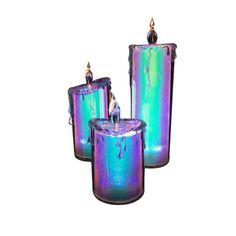 three purple and green holographic candles sitting next to each other on a white background