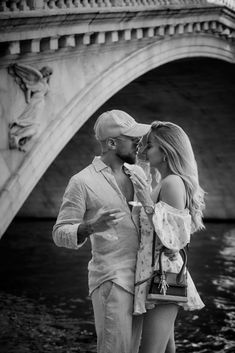 a man and woman standing next to each other in front of a bridge eating ice cream