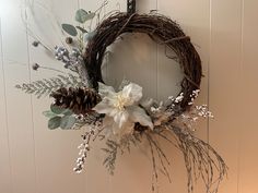 a wreath with white flowers and pine cones hanging on the wall next to a door