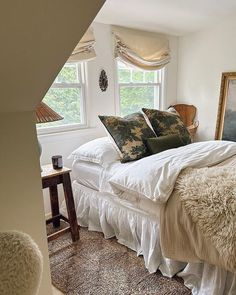 a bed with white sheets and pillows in a bedroom next to a window, rugs on the floor