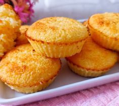 several small muffins on a white plate with pink flowers in the back ground