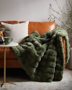 a couch with a blanket on top of it next to a table and potted plant