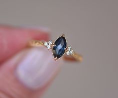 a woman's hand holding an engagement ring with a blue stone and three diamonds