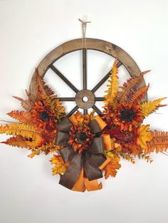 an arrangement of autumn leaves and flowers in front of a wheel on a white wall