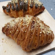 two pastries with chocolate drizzled on them sitting on a cutting board