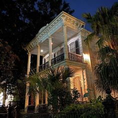 a large white house with columns and balconies lit up at night in front of palm trees