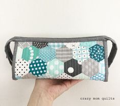 a hand holding up a zippered pouch made out of patchwork fabric with polka dots and hexagons