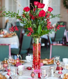 a vase filled with red roses sitting on top of a table covered in plates and silverware