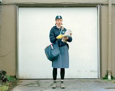 a woman standing in front of a garage door holding a book and bag while looking at the camera