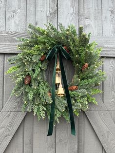 a christmas wreath hanging on the side of a barn door with bells and pine cones