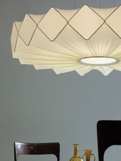 a modern chandelier hanging over a dining room table with two vases on it