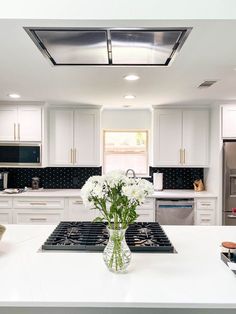 a vase filled with white flowers sitting on top of a kitchen counter next to an oven