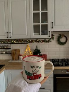 a person holding up a coffee mug with merry bright written on it in a kitchen