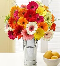 a vase filled with lots of colorful flowers next to a bowl of fruit on a table