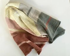 three knitted scarves sitting next to each other on top of a white table