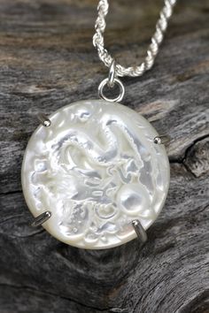 "This unique piece features a round, mother of pearl that has been engraved, revealing a dragon design. The stone sits in a prong setting of sterling silver. The pendant measures 20mm in diameter. The length of the pendant with the silver bail is 1\". It slides around a sterling silver, rope chain with a length of 16\" adjustable up to 18\". History and Metaphysical Properties: Mother of Pearl is an iridescent organic-inorganic composite material that is produced by marine organisms. It is commonly known as nacre and is made of the same materials that pearls are made of. It is composed of aragonite platelets, a form of calcium carbonate. Metaphysically,  it is thought to be the bringer of divine wisdom and intuition. It also has calming effects on the body and emotions. Suupportive of femi Round Pearl Pendant Jewelry From Mother Of Pearl, Round Mother Of Pearl Pendant Jewelry, Spiritual Round Mother Of Pearl Jewelry, Round Dragon Design Jewelry For Gifts, Dragon Design Jewelry For Gift, Dragon Design Jewelry Gift, Engraved Mother Of Pearl Pendant Necklace, Silver Round Mother Of Pearl Jewelry, Silver Mother Of Pearl Round Jewelry