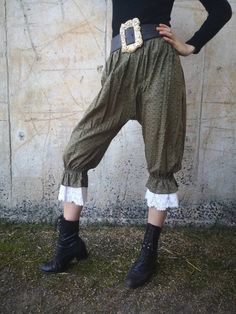 a woman in black shirt and green pants standing next to a wall with her hands on her hips