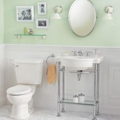 a white toilet sitting next to a sink in a bathroom under a mirror and pictures on the wall