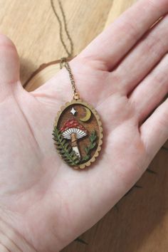 Welcome to our enchanting collection of wooden laser engraved diorama necklaces! Embrace your inner witchy vibes with these magical pieces featuring intricate designs of mushrooms, ferns, trees, and mini magic scenes. Each lightweight necklace is hand painted with care and comes on a beautiful brass chain. - Hand painted wood pieces add a unique touch to each necklace - Mini landscape scenes create a whimsical feel - Brass or gold chain adds a touch of elegance - Water resistant for everyday wea Handmade Magical Charm Necklaces For Gifts, Handmade Magical Pendant Necklace, Mystical Handmade Necklaces For Gifts, Mystical Handmade Necklace For Gifts, Handmade Mystical Necklaces For Gifts, Mystical Handmade Necklace For Gift, Handmade Mystical Necklace For Gift, Nature-inspired Brass Necklace For Gift, Handmade Magical Round Pendant Necklace