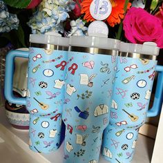 three travel mugs sitting on top of a counter next to flowers and other items