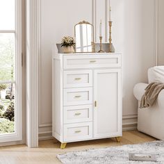 a white cabinet with gold handles and drawers in a living room next to a window