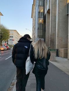 two people walking down the sidewalk in front of a tall building with windows on each side