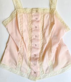 Adorable little vintage  50's/60's pale pink nylon button front camisole top with lace straps Made in USA 100% nylon Marked size 34 and photographed on a size 2/4 dress form. Please use measurements to ensure a proper fit. Pit-to-pit: 16" Top of shoulder-to-hem: 21-1/2" Good vintage condition A NOTE ABOUT MY CLOTHING LISTINGS: I'm very picky when it comes to cut and style so you can rest assured my vintage garments will be WEARABLE mixed in with your modern wardrobe.  I only source high-quality pieces in good to excellent condition and bring them to you at a REASONABLE price.  Unless otherwise noted, all garments are free of rips, tears, stains, missing buttons, etc. NOTE: Please bear that in mind that, when you purchase vintage, it might not be perfect, but it will be authentic.  No retur Fitted Pink Camisole With Lace Top, Pink Fitted Lace Top Camisole, Fitted Lace Top Pink Camisole, Fitted Pink Lace Top With Lace Trim, Vintage Lace Trim Corset For Spring, Fitted Vintage Camisole For Spring, Fitted Coquette Top With Delicate Lace, Vintage Lace Camisole For Spring, Vintage Corset With Lace Trim