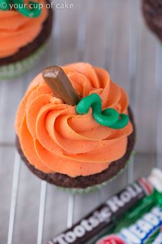 two cupcakes with orange frosting and green icing on a cooling rack