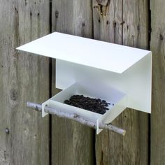 a white bird feeder hanging on a wooden fence with seeds in it's drawer