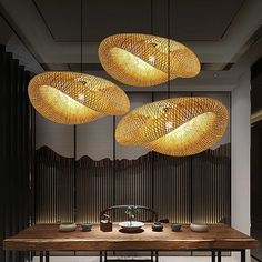 three lights hanging from the ceiling above a table with bowls and cups on it in front of bamboo screens