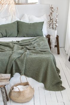 a bed with green blankets and pillows in a bedroom next to a basket on the floor