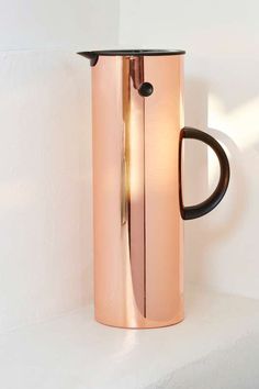 a copper colored coffee pot sitting on top of a white shelf next to a black handle