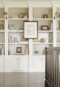 an empty room with bookshelves and pictures on the wall above them, in front of a stair case