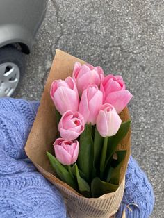 a bouquet of pink tulips sitting on top of a blue blanket next to a gray car