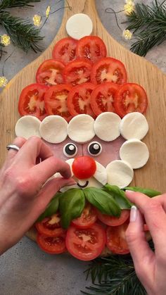 a person making a face made out of tomatoes and cheese on top of a cutting board