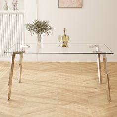 a glass table sitting on top of a wooden floor next to a vase filled with flowers